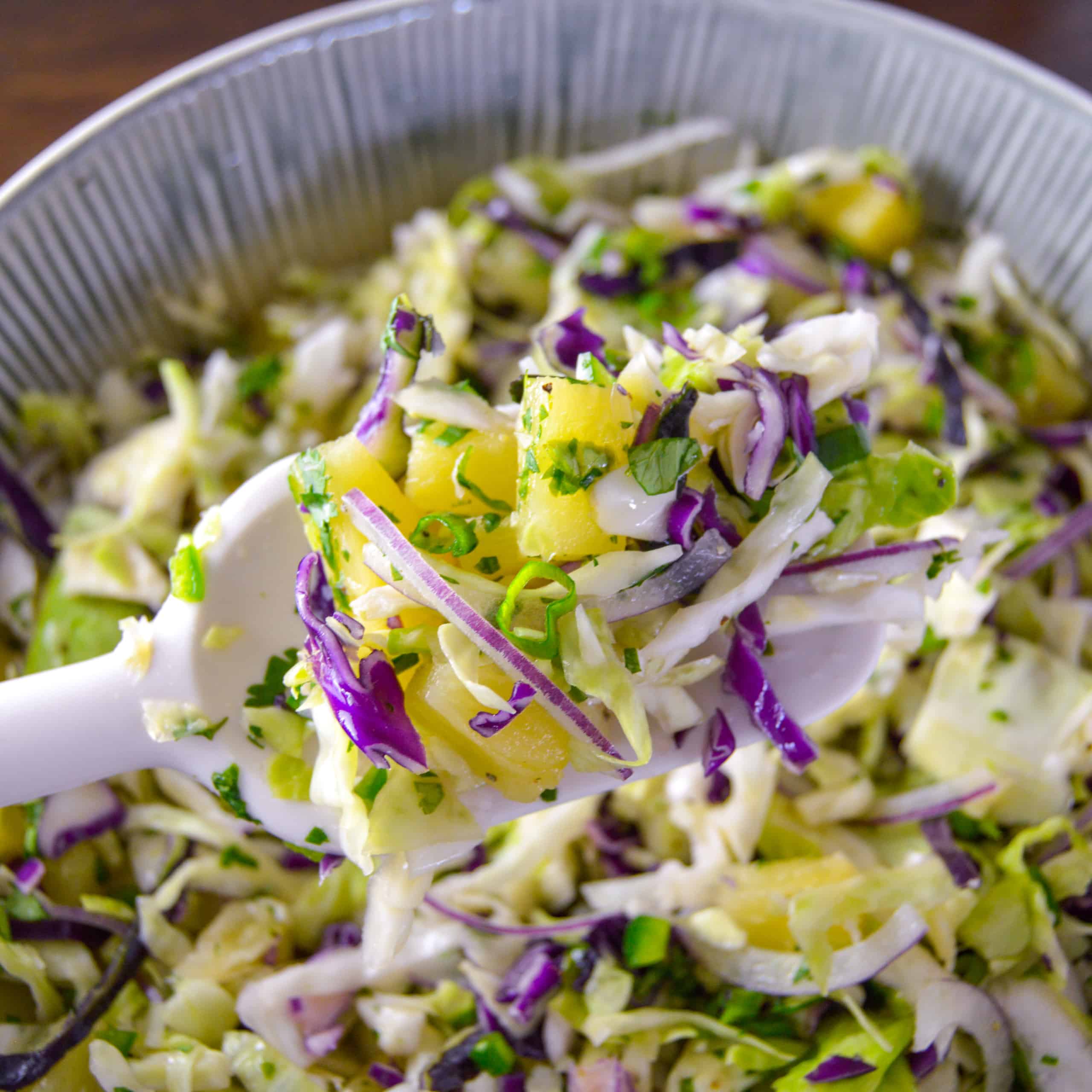 Up close shot of pineapple slaw on white spoon with more slaw in background in ceramic bowl