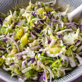 Up close shot of full ceramic bowl of pineapple slaw with jalapeno, red onion and cilantro with white spoon inside slaw
