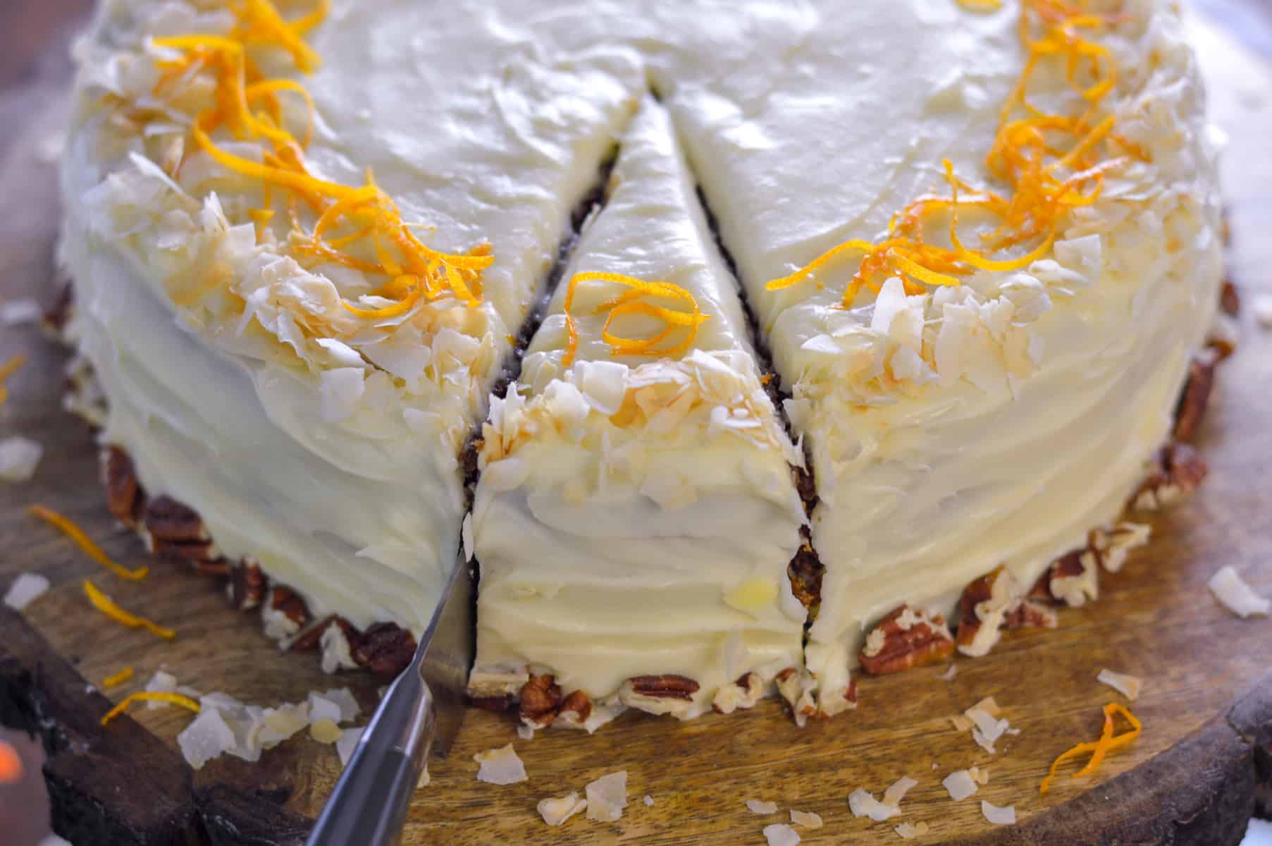 Slice being cut out of carrot cake with grey and silver knife on wooden board