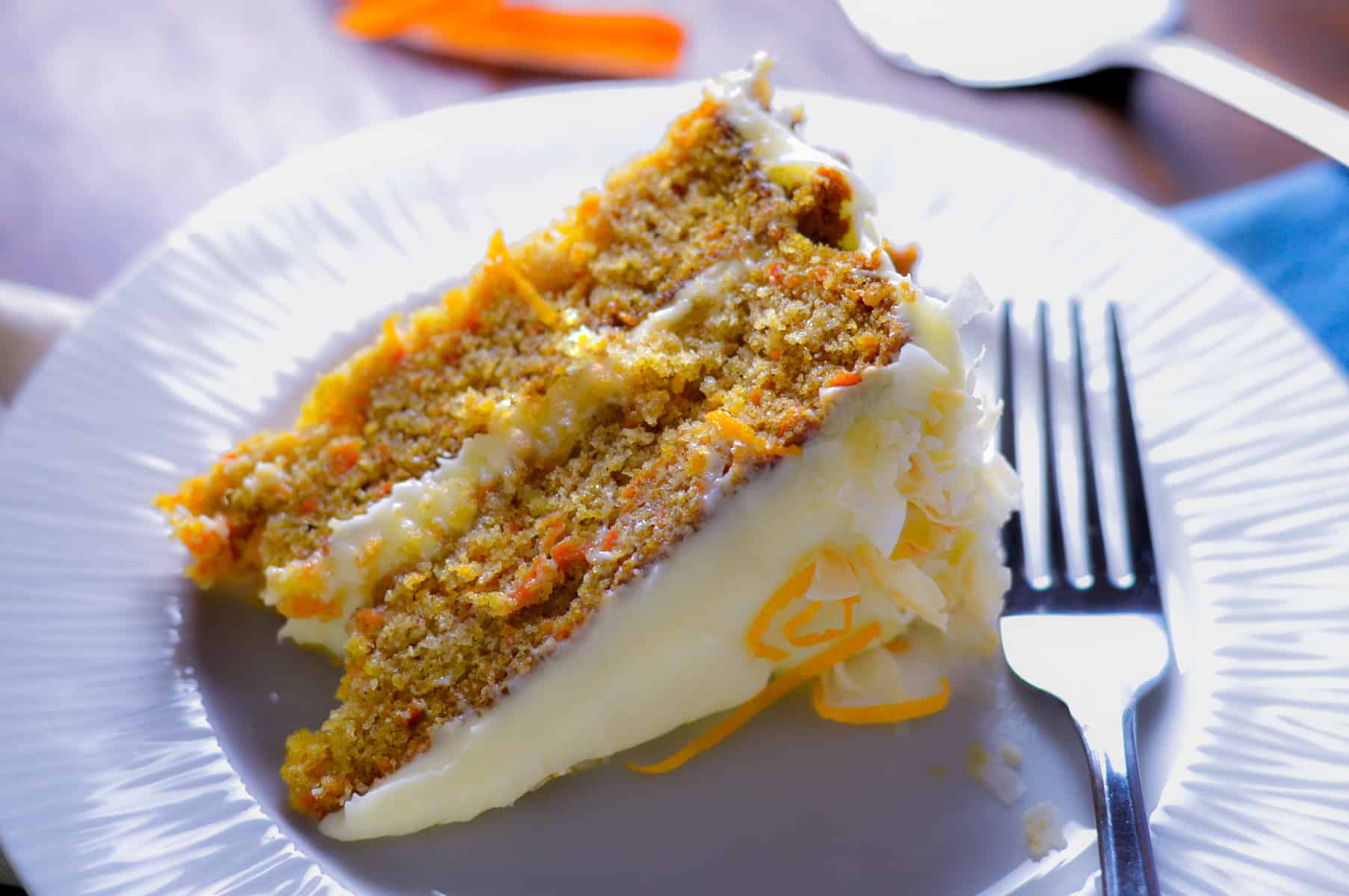 Slice of Orange Carrot Cake on plate laying down on white plate with fork on right