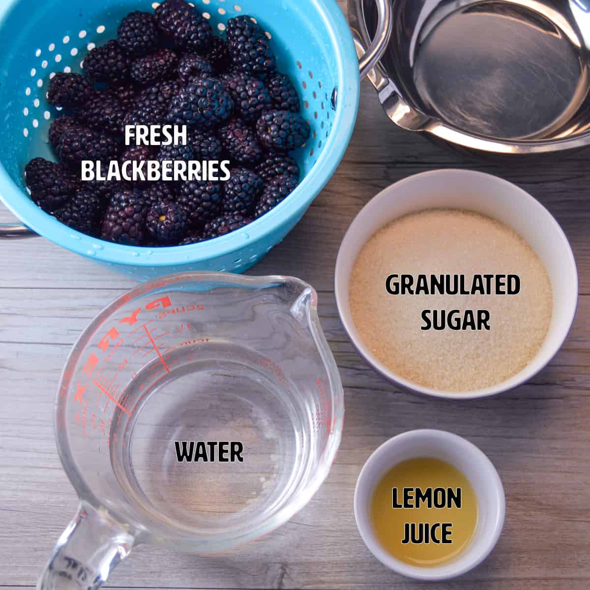 Ingredients for Blackberry Simple Syrup on Counter: fresh blackberries, water, granulated sugar & Lemon juice. Saucepan with pour spout on upper right