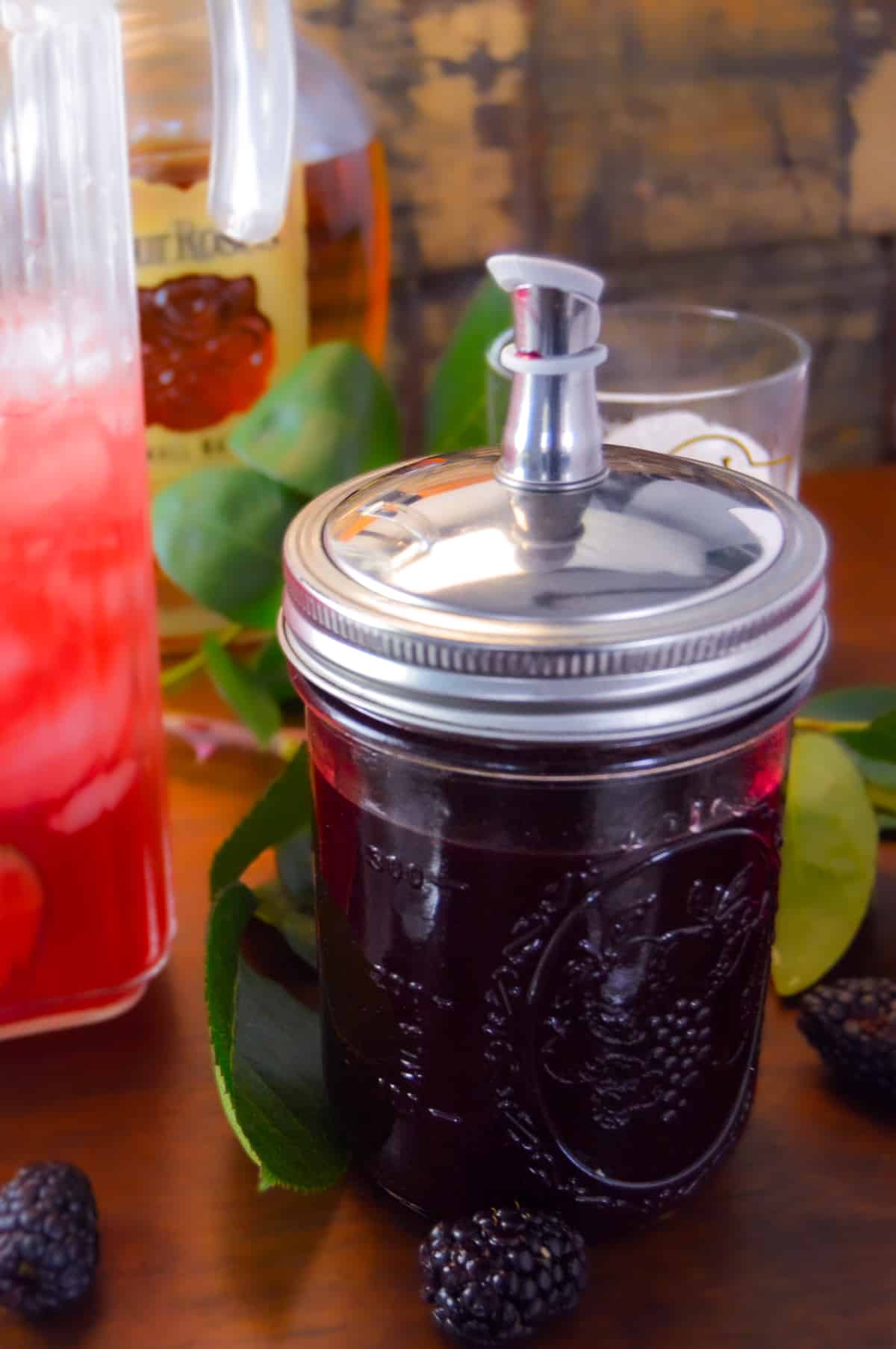 Blackberry Simple Syrup with pour spout top closed and punch with simple syrup in background 
