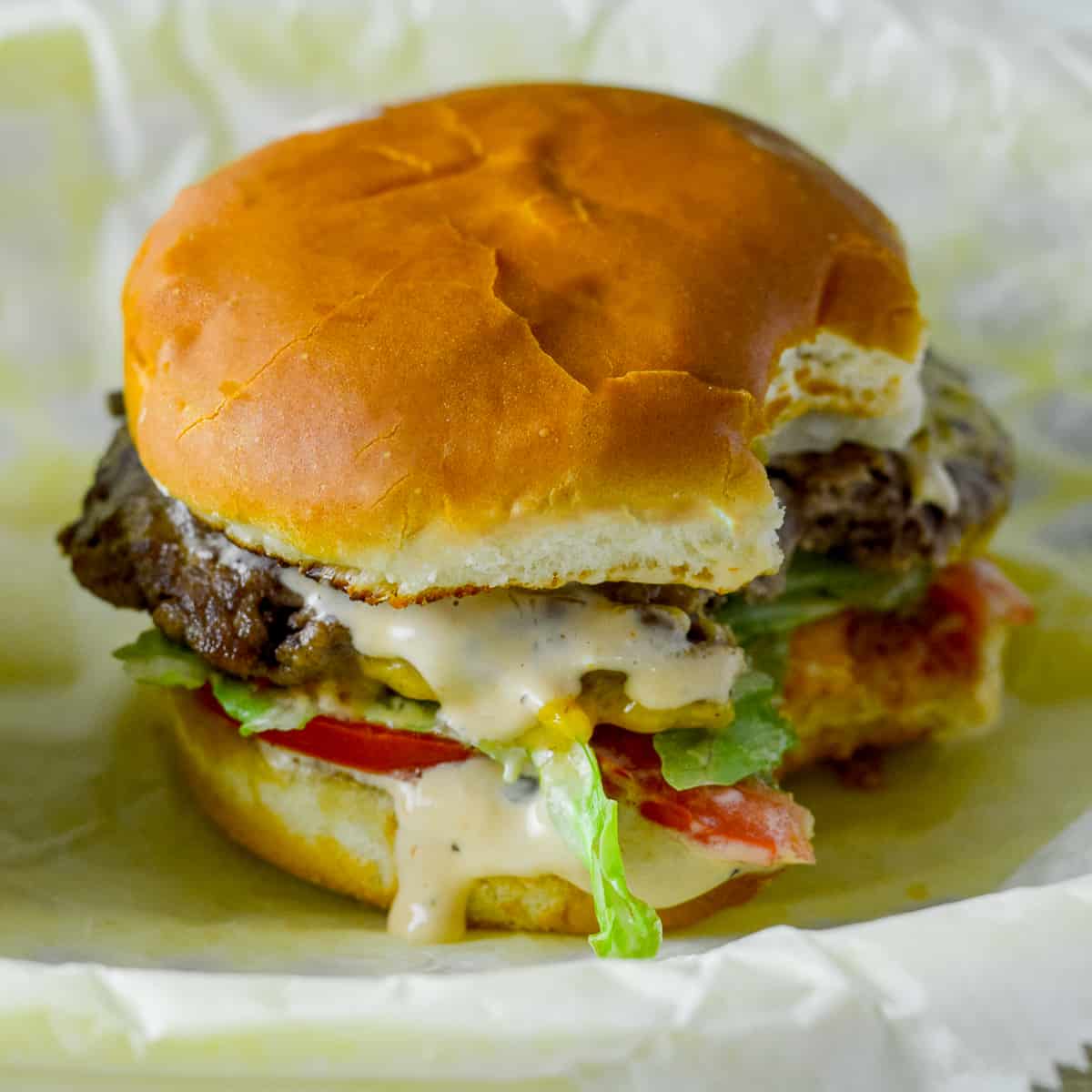 Beef burger with a couple bites in it to look like an In N Out Burger with lettuce, tomato, smashed burger with sauce dripping in a burger basket on top of wax paper
