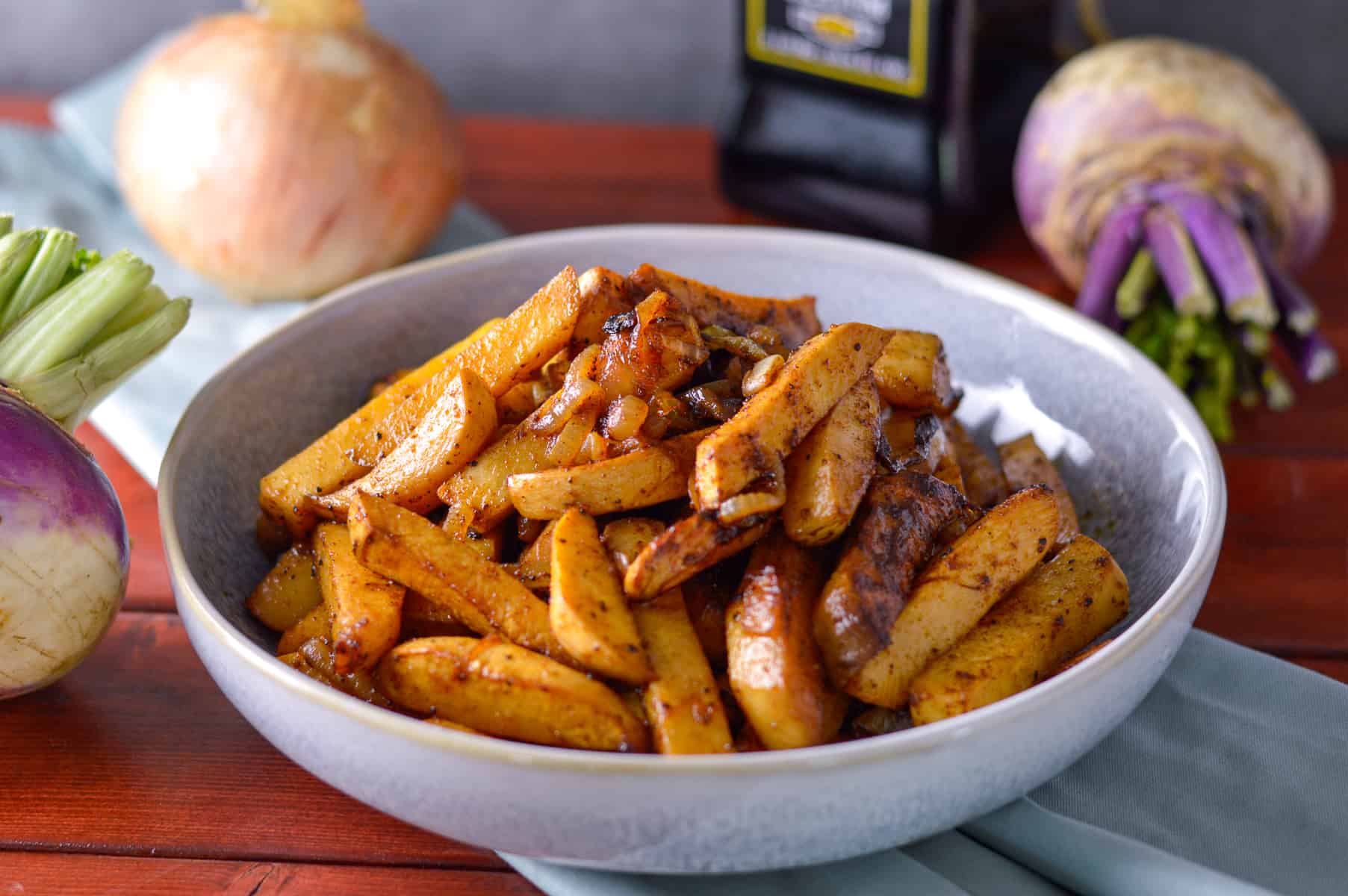 roasted, caramelized turnips cut into fat fries in serving bowl with 2 purple top turnips on the side and behind, onion and balsamic vinegar bottle in background