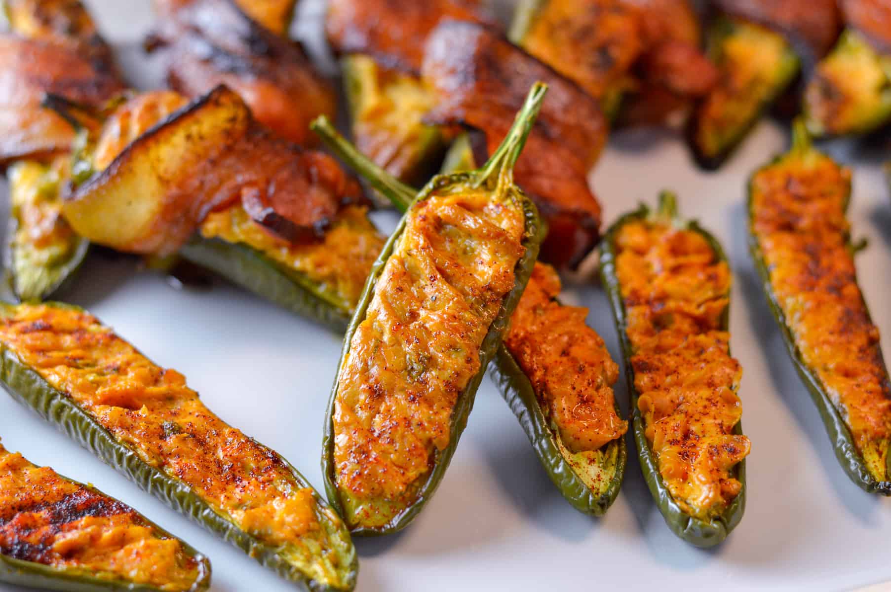 Plain jalapeno popper shown in front with bacon-wrapped in the background on a while platter