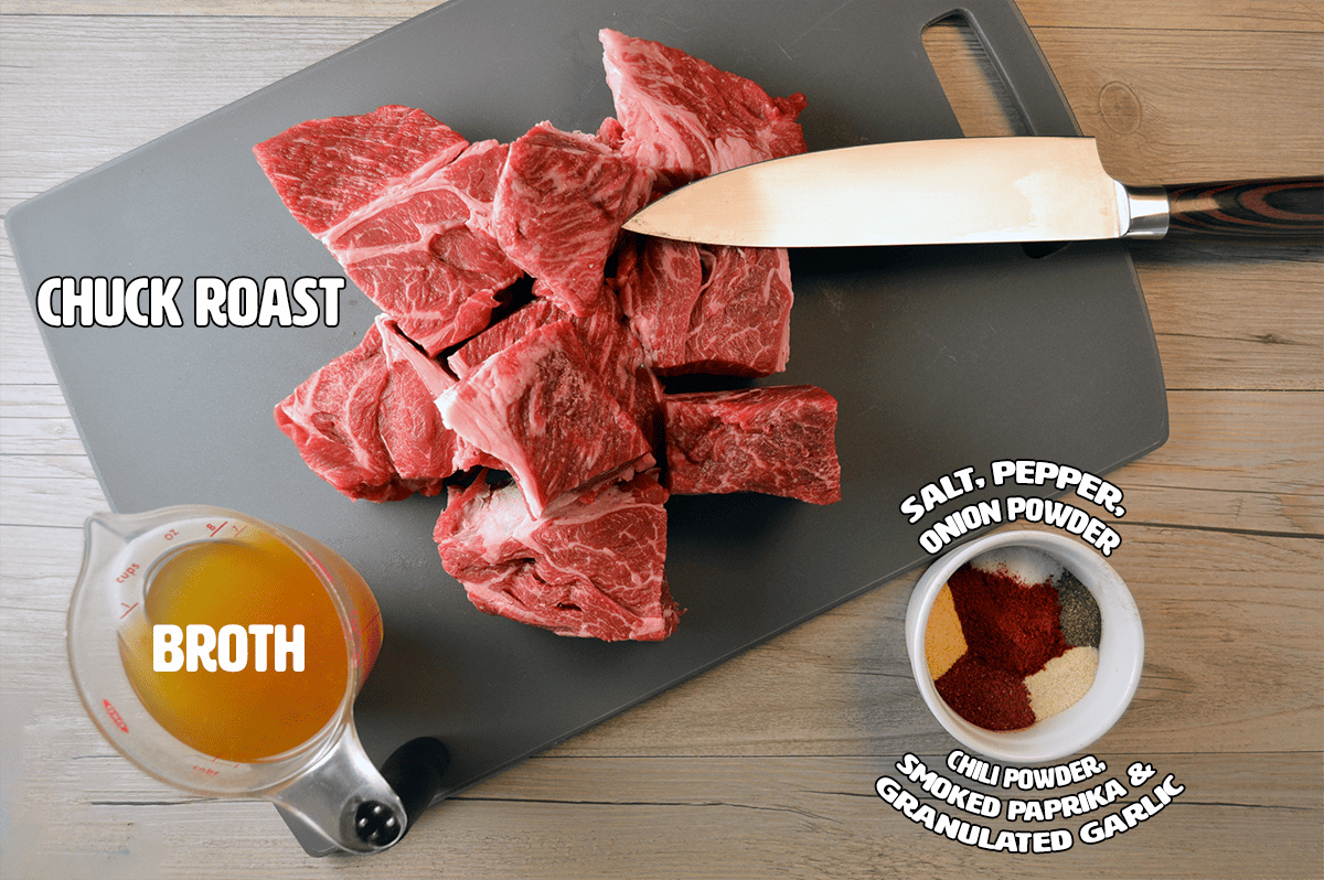 Multi-purpose Shredded Beef Ingredients on grey cutting board with knife and chuck roast chunks with cup of vegetable broth 