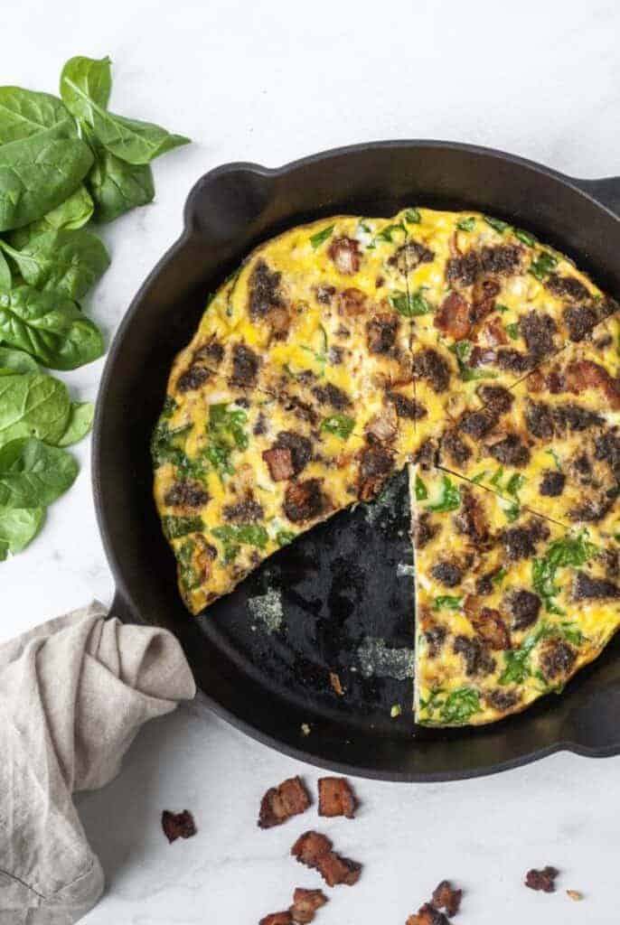 Paleo Frittata with Spinach from Organically Addison in Black Cast iron skillet with bacon and towel wrapped around handle