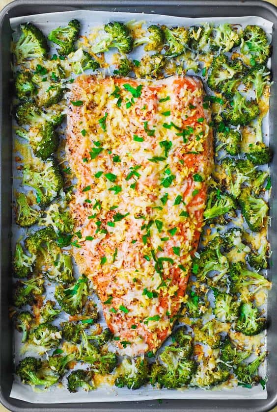 Sheet Pan Salmon and broccoli with garlic and parmesan on a sheet pan lined with parchment paper, toped with green onion and cheese