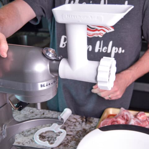 Kitchen Aid Stand Mixer with grinder attachment on and Josh in the background with a baking sheet with pork chunks.