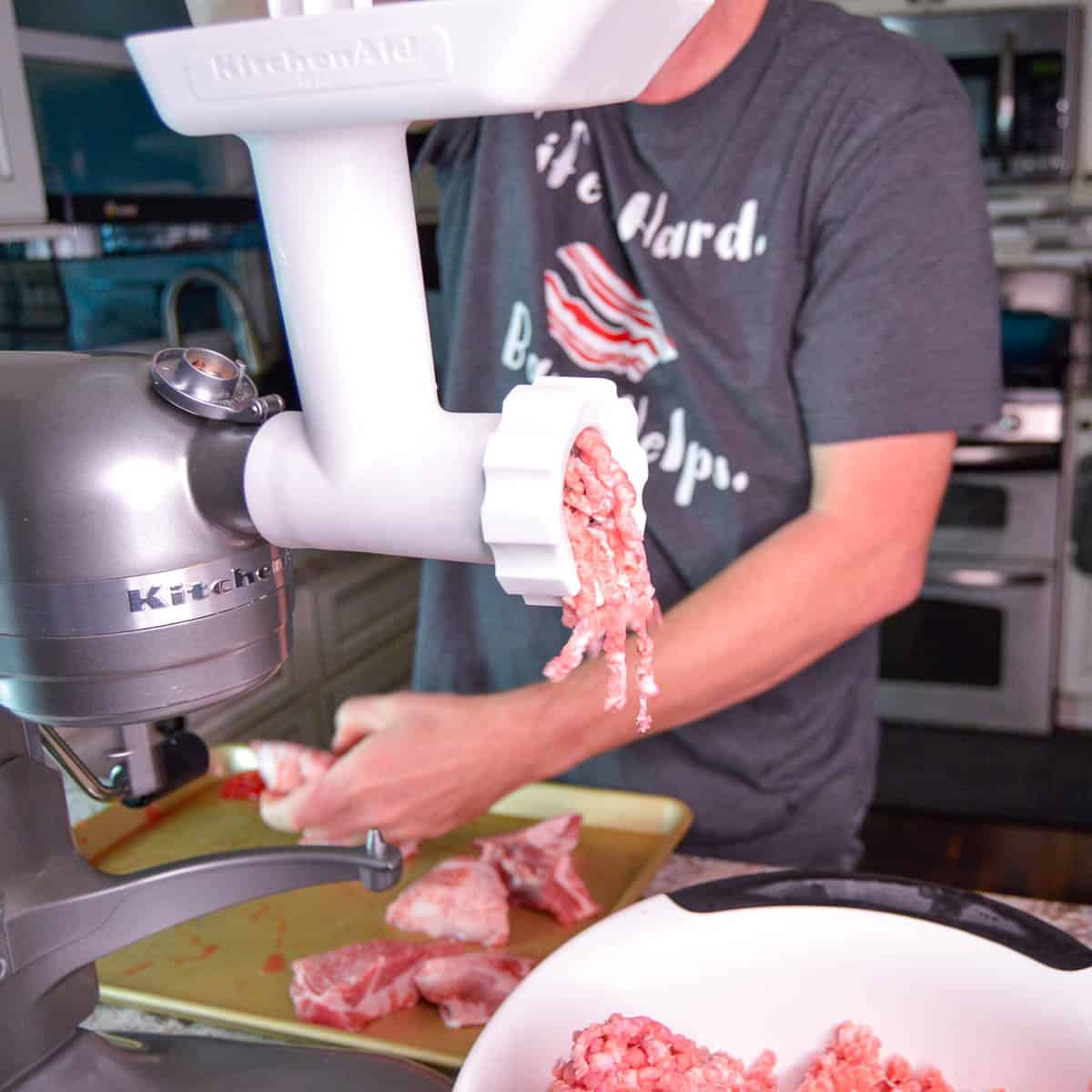 View of grinding pork with grinder attachment on stand mixer with ground pork going into a large white bowl