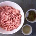 Ground Pork in white bowl with seasonings on side with apple cider vinegar
