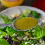 Apple Cider Vinaigrette Salad Dressing on a spoon with dressed salad and apple cider vinegar below