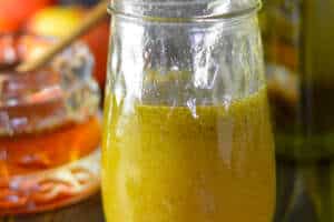 Apple cider vinaigrette salad dressing in a mason jar with a small spoon; honey and olive oil and apples in the background
