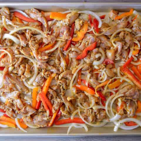 raw marinated chicken mixed in with onions and peppers on sheet pan