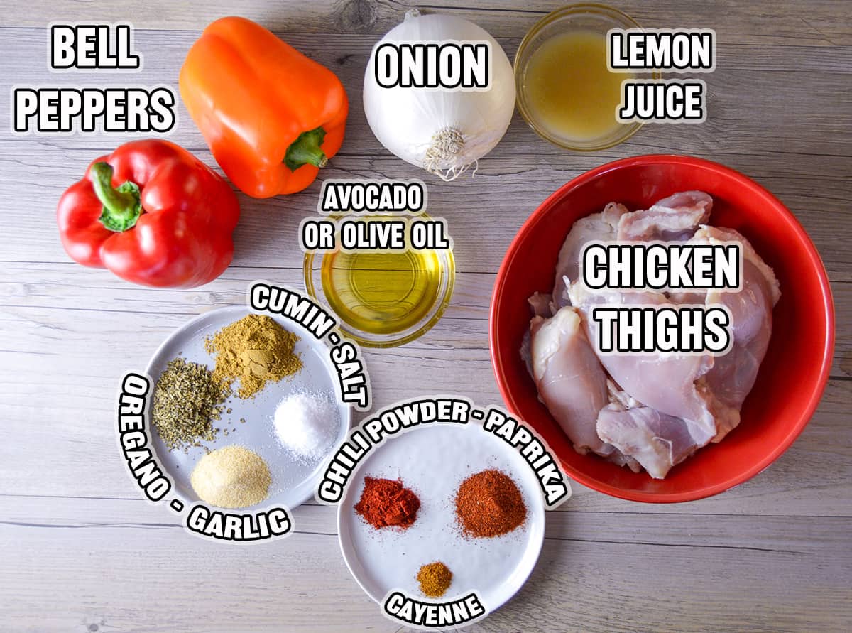 Ingredients shown on grey wooden board for sheet pan chicken fajitas: chicken thighs, onion, bell peppers, oil, lemon juice and spices