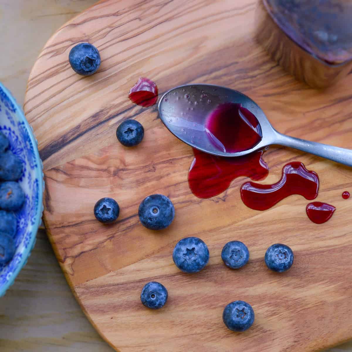 Blueberry Simple Syrup on silver spoon spilled over wooden cutting board with fresh blueberries 