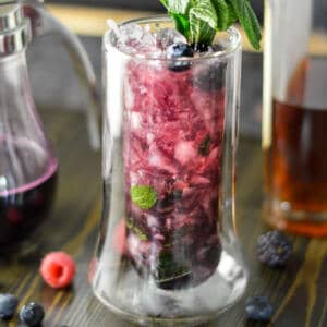 Berry Mint Julep in tall highball glass with mint sprigs and some berries with a berry simple syrup on the side with a bottle of bourbon
