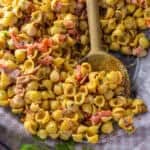 Close up image of roasted pepper and bacon spicy pasta salad in a large clear serving bowl over red and white napkin