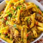 Over top of serving bowl view of pulled pork penne pasta dish with wooden serving spoon over red and white napkin