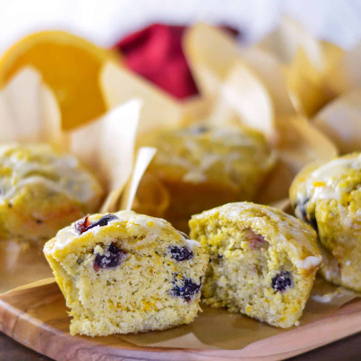 Cranberry orange muffins with orange glaze on wooden cutting board with 1 muffin cut in half and oth