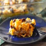 Bourbon Bread Pudding on blue plate with copper fork on green napkin in front of baking dish with baked bread pudding.