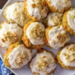 Carrot cake cookies with frosting and crushed pecans on a white plate with a blue and white napkin underneath.