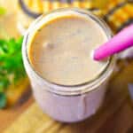 3/4 Over top view of Russian dressing in a mason jar on a wooden cutting board next to bunch of fresh parsley, a knife and a Reuben sandwich.