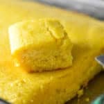 moist buttermilk cornbread in a glass dish with a square sitting on top next to a small metal spatula