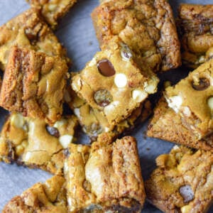 Chocolate chip blondies with dark and white chips on a grey ceramic plate randomly stacked and dispersed