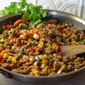 Ground Beef Skillet stir fry with a wooden spoon, some parsley, a yellow bell pepper and a bottle of olive oil