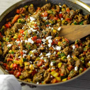 Close up view of Mediterranean ground beef skillet in a skillet with a wooden spoon and a white napkin on the handle